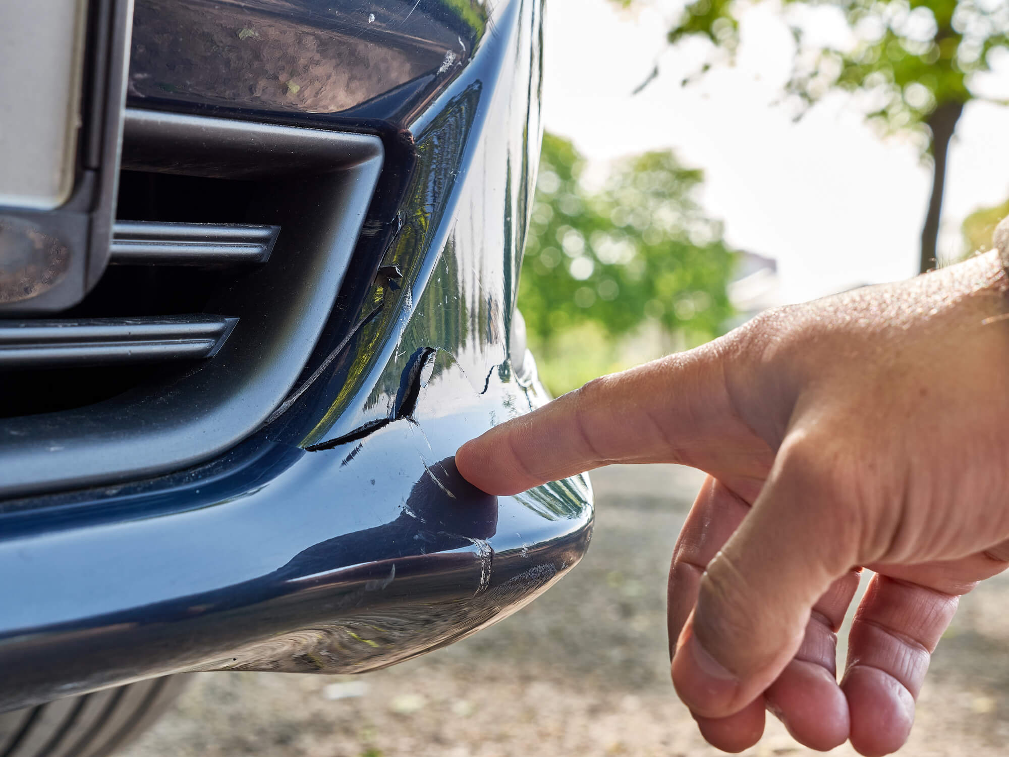 Finger zeigt auf Kratzer am Auto